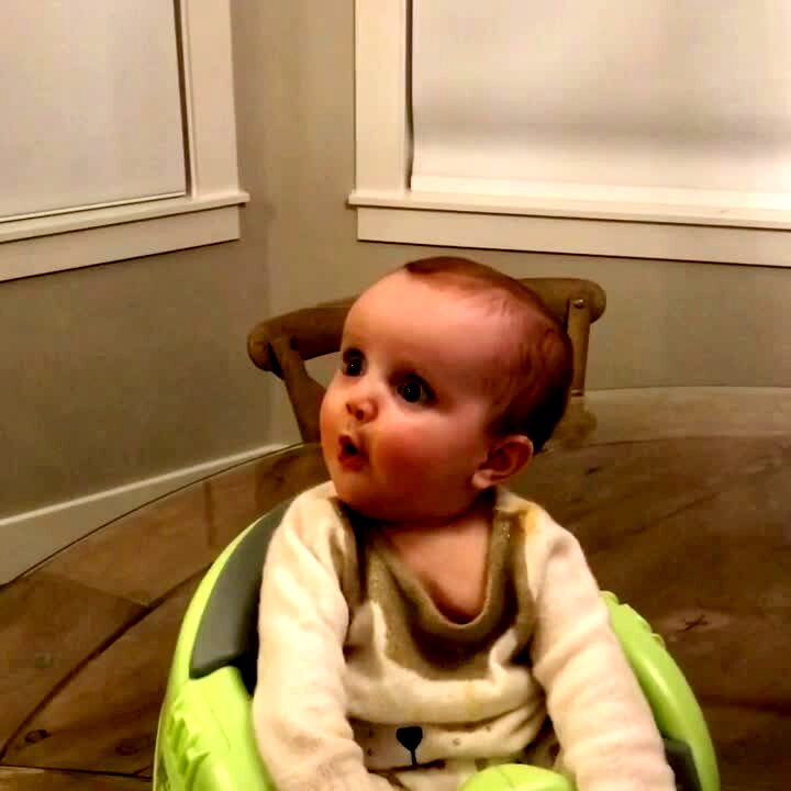 Video thumbnail showing: A baby girl makes an excited face when her grandma holds a new dress in front of her in the living room.