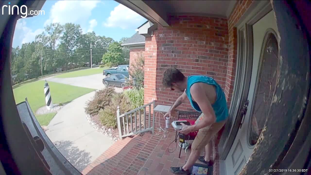 Video thumbnail showing: A young man walks up a flight of stairs to his house and drops a drink, but he catches it before it spills. He sets it down and adjusts pillows on a chair, then knocks it over with the pillow and spills it. Security footage.